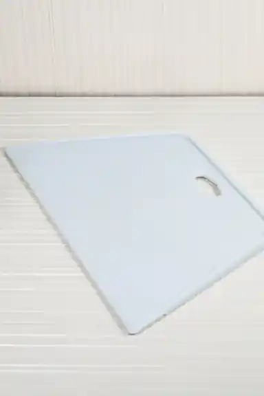 Angled view of white plastic wallpaper squeegee lying flat showing its trapezoidal smoothing edge