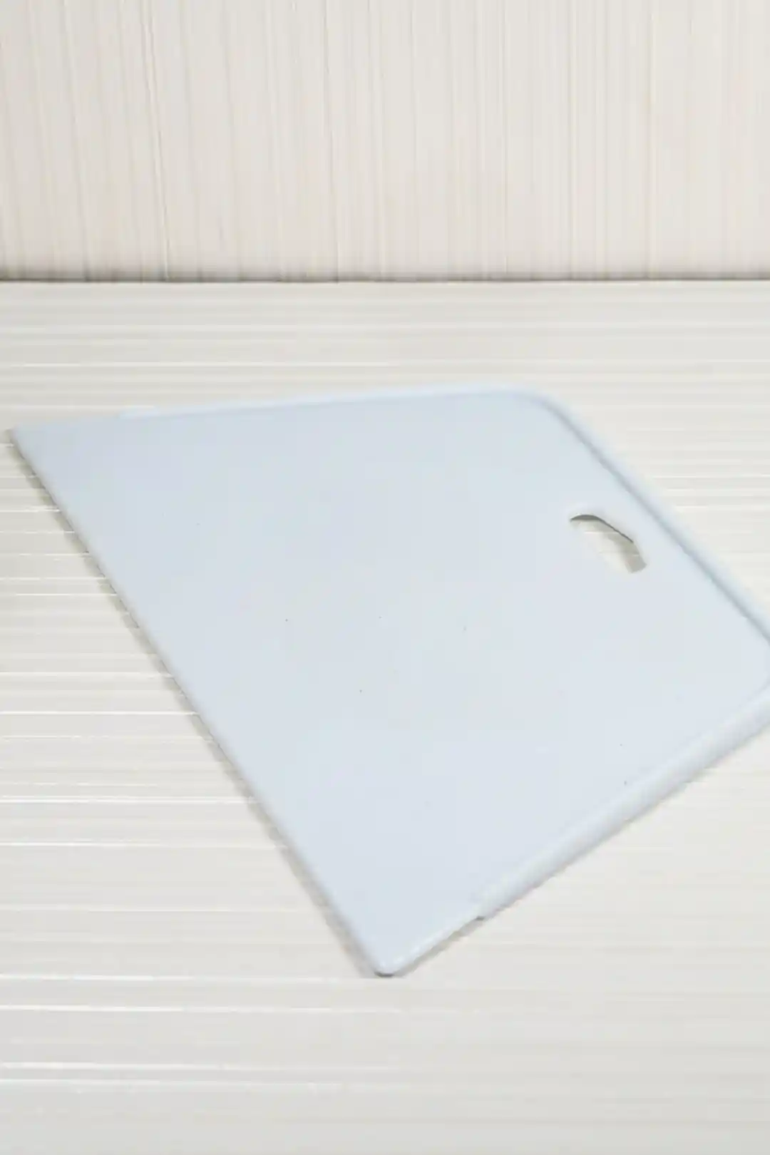 Angled view of white plastic wallpaper squeegee lying flat showing its trapezoidal smoothing edge