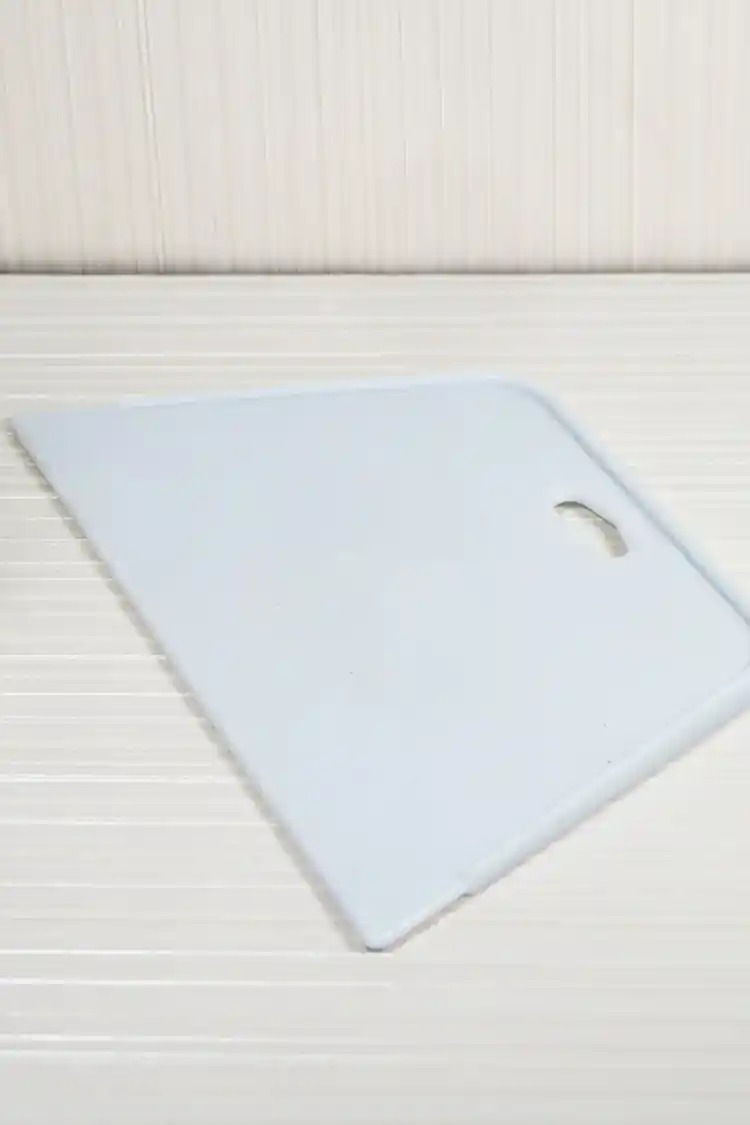 Angled view of white plastic wallpaper squeegee lying flat showing its trapezoidal smoothing edge